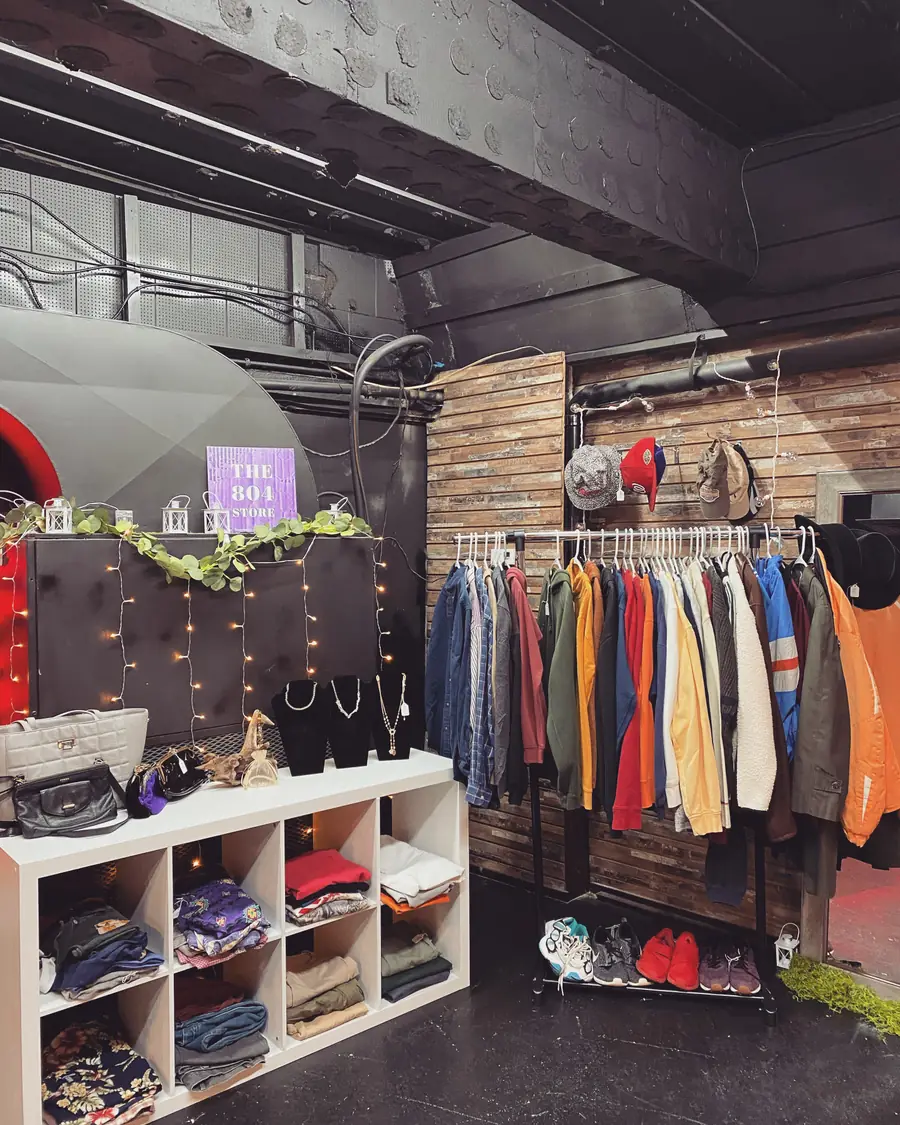 A corner shop setup with cubbies of folded clothes, a rack of jackets, and string lights under The804Store sign